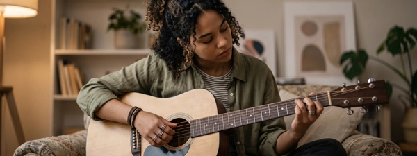 A young woman playing an acoustic
guitar at home, symbolizing the emotional regulation, resilience, and personal growth achieved through
specialized counseling and therapy services for children, teens, and adults.