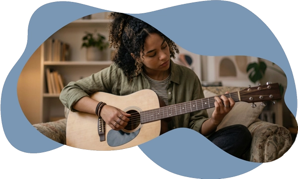 A young woman with curly hair playing an acoustic guitar on a sofa, representing how psychotherapy
helps individuals navigate neurodivergence, heal from burnout, and live with intention.